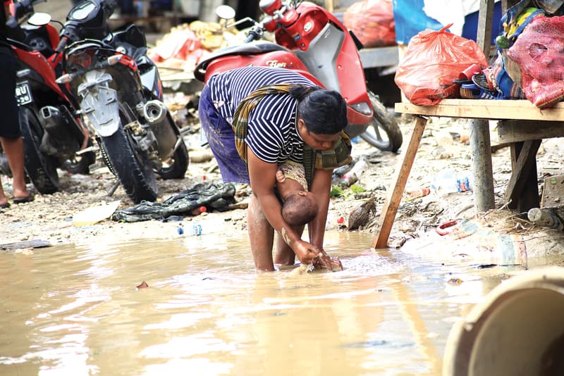 BERSIHKAN DIRI: Seorang ibu menggendong bayi sambil membersihkan tangan dengan air lumpur di lokasi bekas banjir di Kota Jayapura, Papua kemarin (8/1). (EFLIAN/CENDERAWASIH POS) - Image
